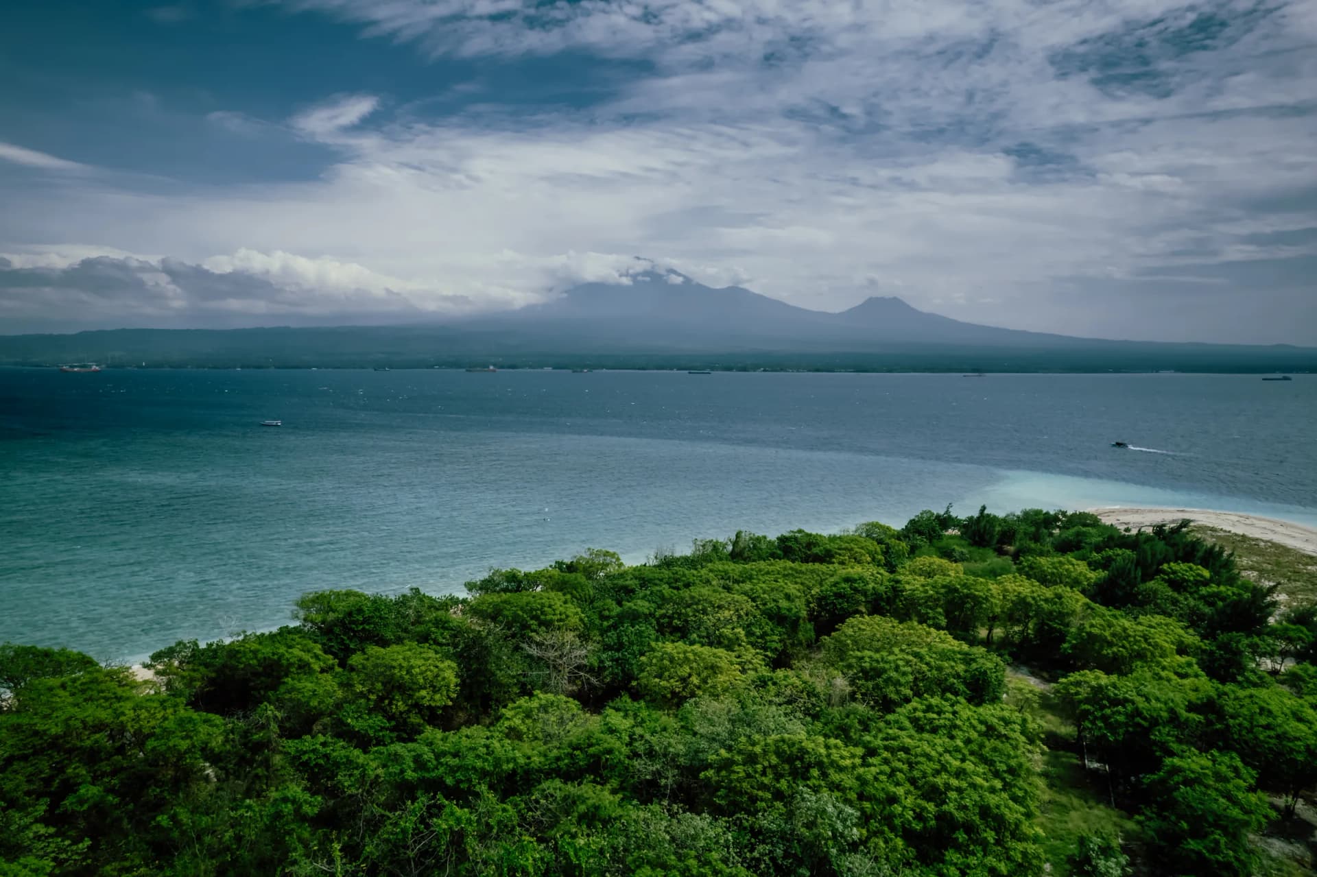 View over Tabuhan Island's forest to the sea and distant volcanoes