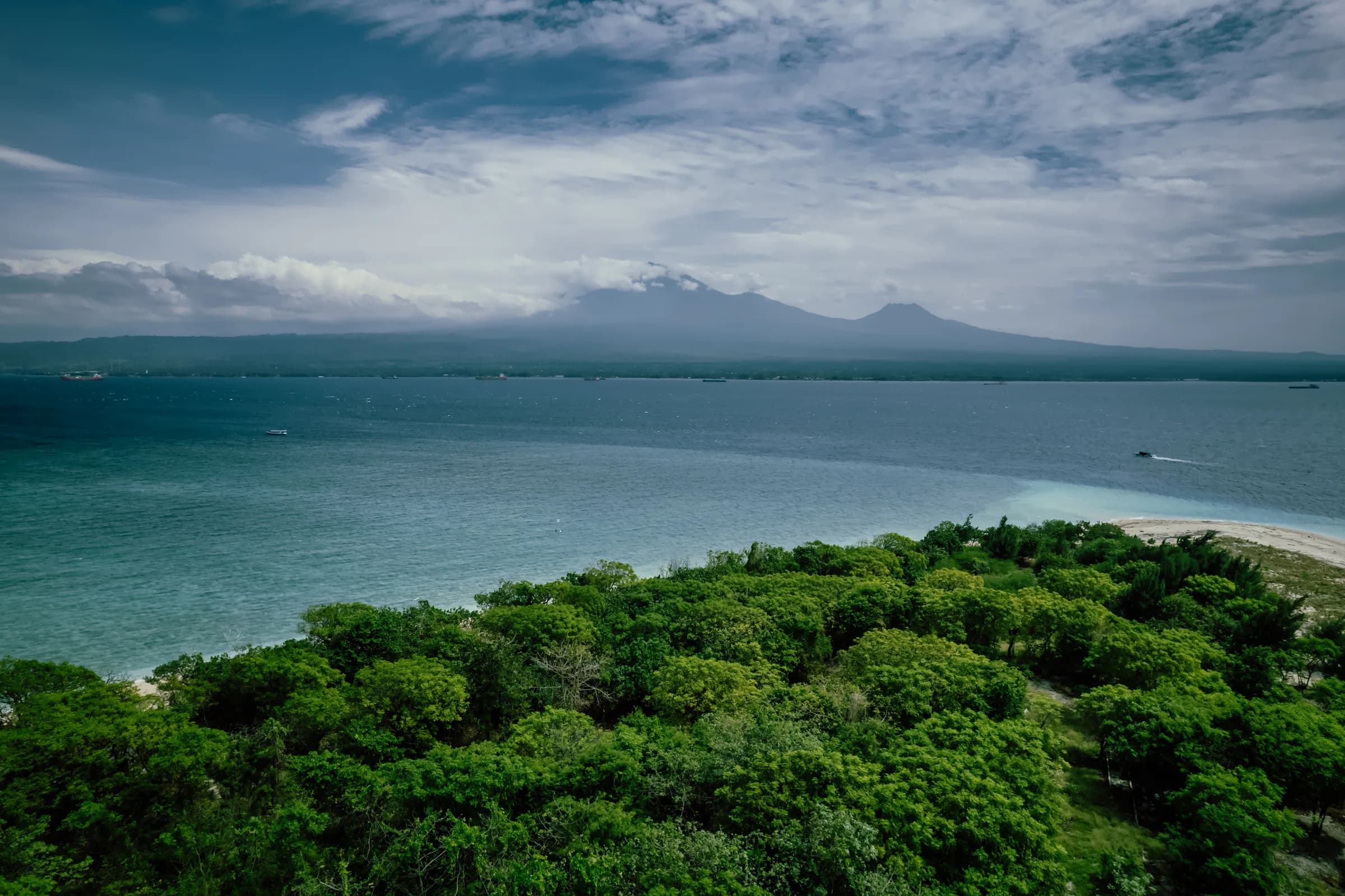 View over Tabuhan Island's forest to the sea and distant volcanoes